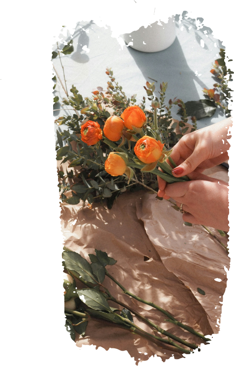 Mains arrangeant des fleurs orange sur une toile beige.