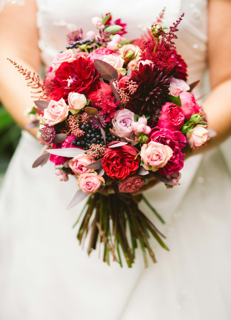 Mariée tenant un bouquet de fleurs rouges et roses.